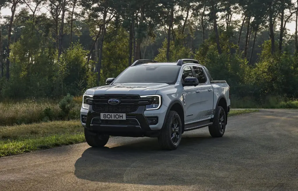 Hvit pickup truck på skogkledd vei.