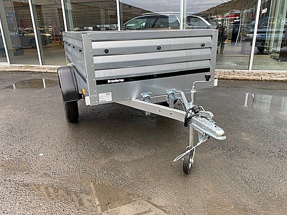 Grå tilhenger parkert foran bilforretning.