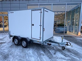 Hvit tilhenger utenfor bygning om vinteren